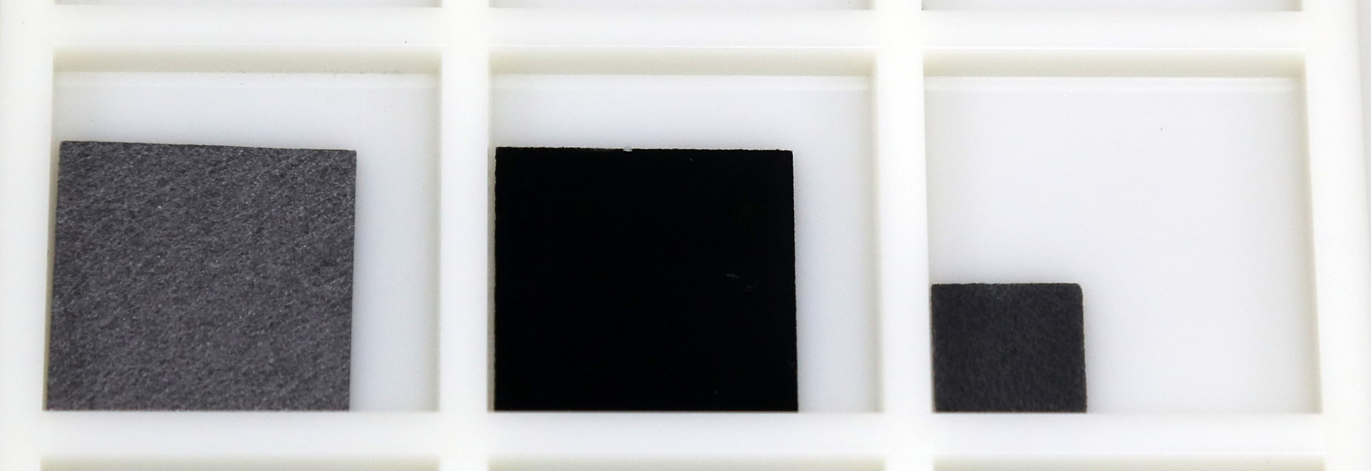 写真左が、炭素繊維を貼り合わせて作られる「カーボンペーパー」の試料片。真ん中の写真が「（仮称）マリモカーボンシート」だ。これは「カーボンペーパー」を形作る繊維にさらに微細な繊維状ナノ炭素を合成させた複合材料で、黒色をしている。大きさ は2センチメートル角。写真右側は、試験的に「（仮称）マリモカーボンシート」にパラジウムを固定化（担持）した試料片